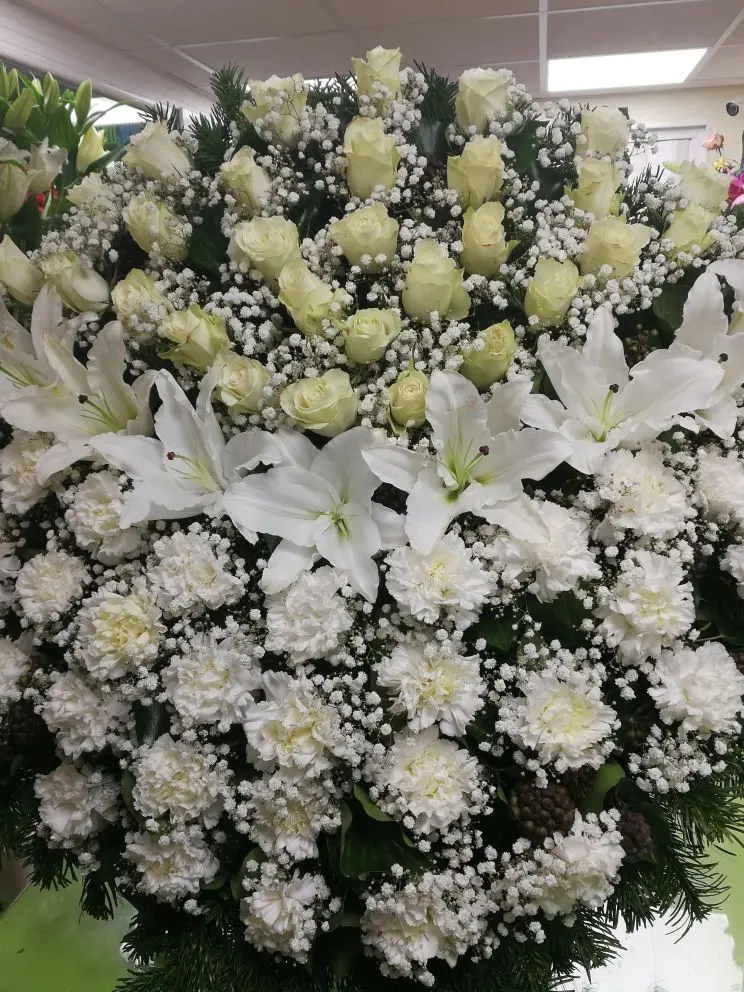 Álló koszorú (80 cm) fehér rózsával, liliommal és szegfűvel, bő rezgő díszítéssel – klasszikus, elegáns temetési kompozíció. Nefelejcs Virágüzlet.